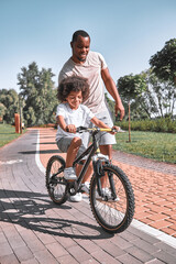 Caring father supporting his kid in learning how to cycle