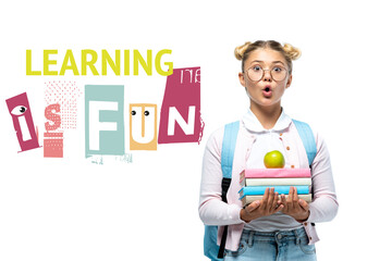 Shocked schoolgirl holding apple and books near learning is fun lettering on white