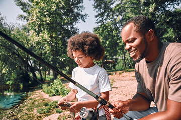 Happy child and his dad fishing on beautiful day outdoors