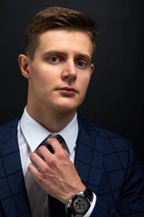 caucasian business man straighten a tie isolated over black background. young guy in formal suit preparing for meeting
