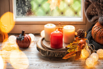 Pumpkins on the sill window, rainy weather outside. Autumn seasonal decor composition with candles light. Cozy home concept. Copy space for your text