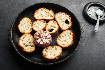 Fresh crispy crostini baguette slices with baked garlic, butter and cheese in a baking dish on a dark background. Top view. Selective focus