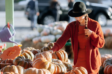Portrait of happy woman choosing ripe orange pumpkin on farmers market in brown sweater, dress. Cozy autumn vibes Halloween, Thanksgiving day