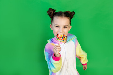 a cute girl is licking a large Lollipop in a bright suit on a green isolated background. Space for text.