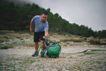 A man is grabbing his green bag from the floor during a hike