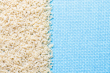 Baby pasta in the form of letters on a blue background with copy space. The background has a burlap texture. Top view. Close-up.