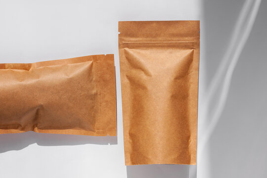 Brown kraft paper pouch bags with coffee beans top view with shadow isolated on white background. Packaging for foods and goods template mockup. Pack with clasp for tea leaves,weight products flat lay