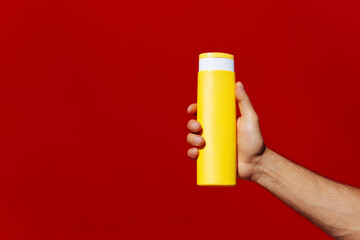 Man holding a yellow bottle isolated on red background.Man hand holding sun lotion bottle (on red background)