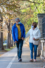 Mature couple with masks walking in the park during coronavirus. An elderly couple in protective masks walking in the Park, a walk in the fresh air after quarantine.