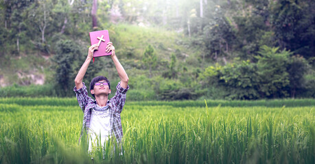 Young man standing in rice field holding and raise up the Cross and bible, Christian concept.