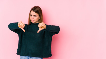 Young caucasian woman isolated on pink background showing thumb down, disappointment concept.