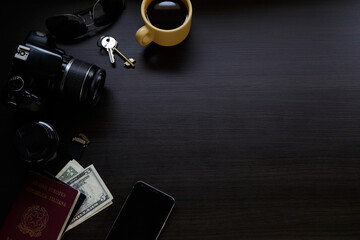 Top view of dark wooden desk with reflex digital camera, an smartphone, passport, coffee cup and money.  Traveler table concept. Copy space.