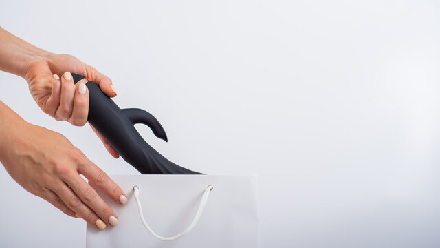 A woman makes a purchase and puts a dildo in a bag on a white background. Close-up of female hands with a black vibrator