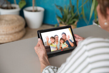 Elderly woman making video call with adult children and grandchildren on digital tablet at home. Distancing. copy space.