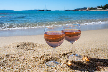 Two glasses of local rose wine on white sandy beach and blue Mediterranean sea on background, near Le Lavandou, Provence, France