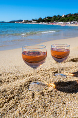 Two glasses of local rose wine on white sandy beach and blue Mediterranean sea on background, near Le Lavandou, Provence, France