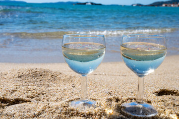 Two glasses of local dry white wine on white sandy beach and blue Mediterranean sea on background, near Le Lavandou, Provence, France