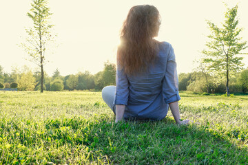 Young woman sitting on the grass. Golden sunset in the background.