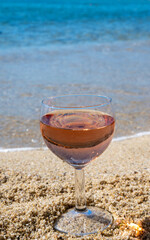 Glass of local rose wine on white sandy beach and blue Mediterranean sea on background, near Le Lavandou, Provence, France