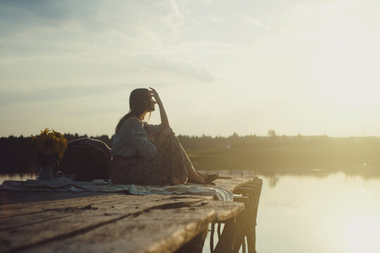 Attractive young girl in stylish clothing posing on a wooden Pier and Dreaming. Photo with Film and Grain Effect