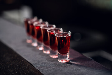 a row of shots with red liquor on the bar on the fabric close up.