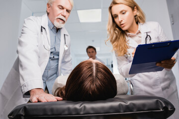 Selective focus of patient lying on stretcher near doctors with clipboard in clinic