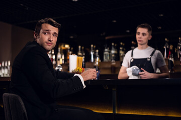 a young man drinks a cocktail at the bar, communicates with the bartender.