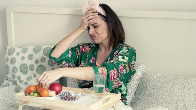 Sick, unhappy woman in pyjamas sitting in bed, 4K 
