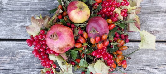 Autumn harvest: red fruits and berries: pomegranate, apples, viburnum, rose hips on the background of a wooden table. 