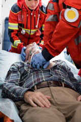 Fototapeta na wymiar Selective focus of paramedics in latex gloves doing cardiopulmonary resuscitation to patient in oxygen mask