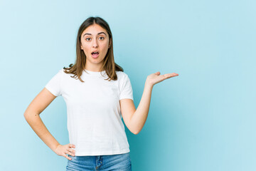 Young caucasian woman impressed holding copy space on palm.