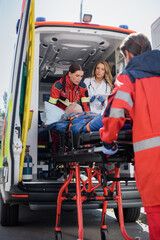 Selective focus of paramedic carrying stretcher with patient near doctor with digital tablet in...