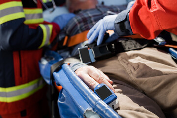 Fototapeta na wymiar Cropped view of patient with heart rate monitor lying on stretcher near paramedics