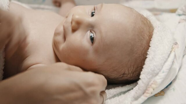 A little baby lying in bed and his mother cleaning his ears with q-tips