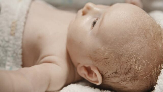 A little baby lying in bed and his parent cleaning his ears with q-tips