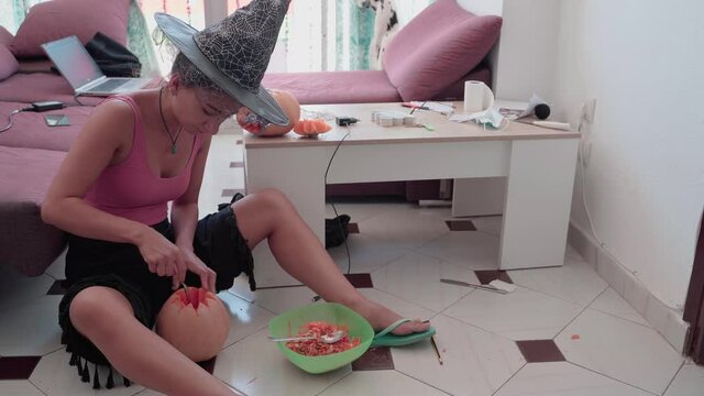 Woman with witch hat carving pumpkin for Halloween. Static, high angle