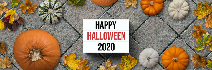 autumn decoration with pumpkins and colorful leaves and message HALLOWEEN 2020 on stone pavement...