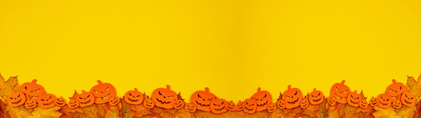 HALLOWEEN background banner wide panoramic panorama template -Scary carved luminous cartoon wooden orange pumpkins and isolated on yellow orange paper texture and fallen autumnal autumn leaves 