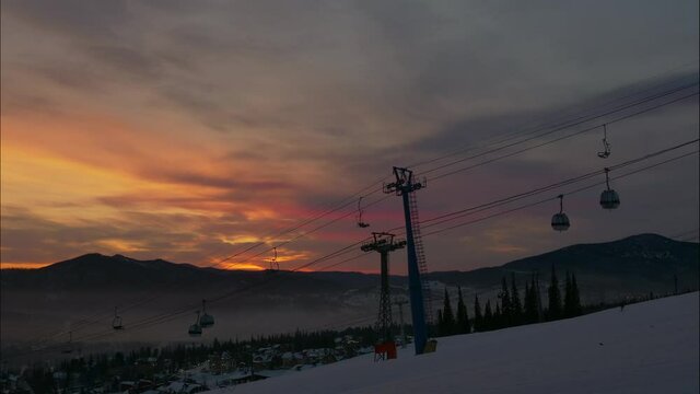 silhouette of poma lift with moving cabins on cables above mountain slope at ski resort from sunrise till day in winter timelapse