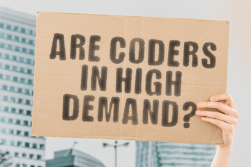 The question " Are coders in high demand? " on a banner in men's hand with blurred background. Programming. Computer science. Education. Technology. Specialist. Occupation. Job. Work. Employee