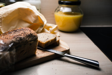 Whole grain bread full of chia seeds sliced on wooden cutting board and jar with homemade ghee in out of focus background