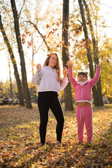 Mom and daughter throwing up dead leaves in autumn park