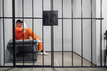Solitary cell with a criminal in an orange robe in an asian prison. Copy space. Sad emotions of a young guy