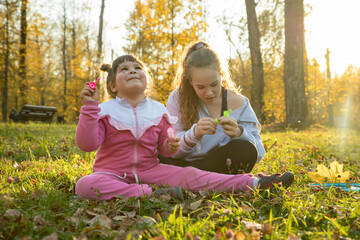 Fototapeta premium Two sisters in autumn park - a little girl sitting on the ground and another sitting next to her