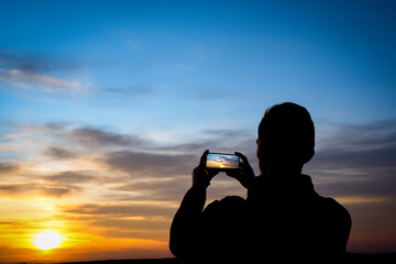 Silhouette of young man shoots sunset on phone, smartphone. Travel, walking.