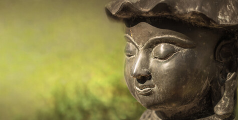 Fototapeta na wymiar Buddha Face in Sunlight with Blurred Green Background