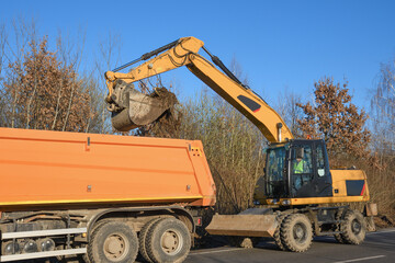 A bucket excavator clears the roadside. Road works. Laying a new road. Loading excavator clay and stones