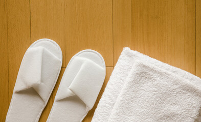 Flat lay view of pair of white new clean spa disposable spa slippers and white clean towels in stack. Copy space on wood background. Beauty care lifestyle.