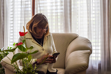 older woman in the comfort of her home using her smartphone to connect with new technologies