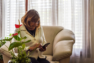 older woman in the comfort of her home using her smartphone to connect with new technologies